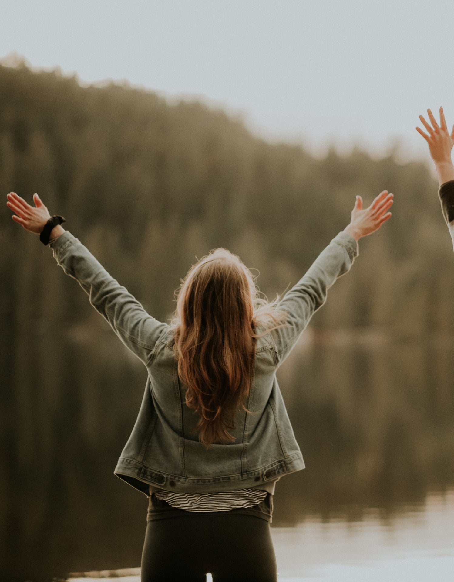 Zwei Frauen vor einem See heben ihre Arme glücklich in die Luft